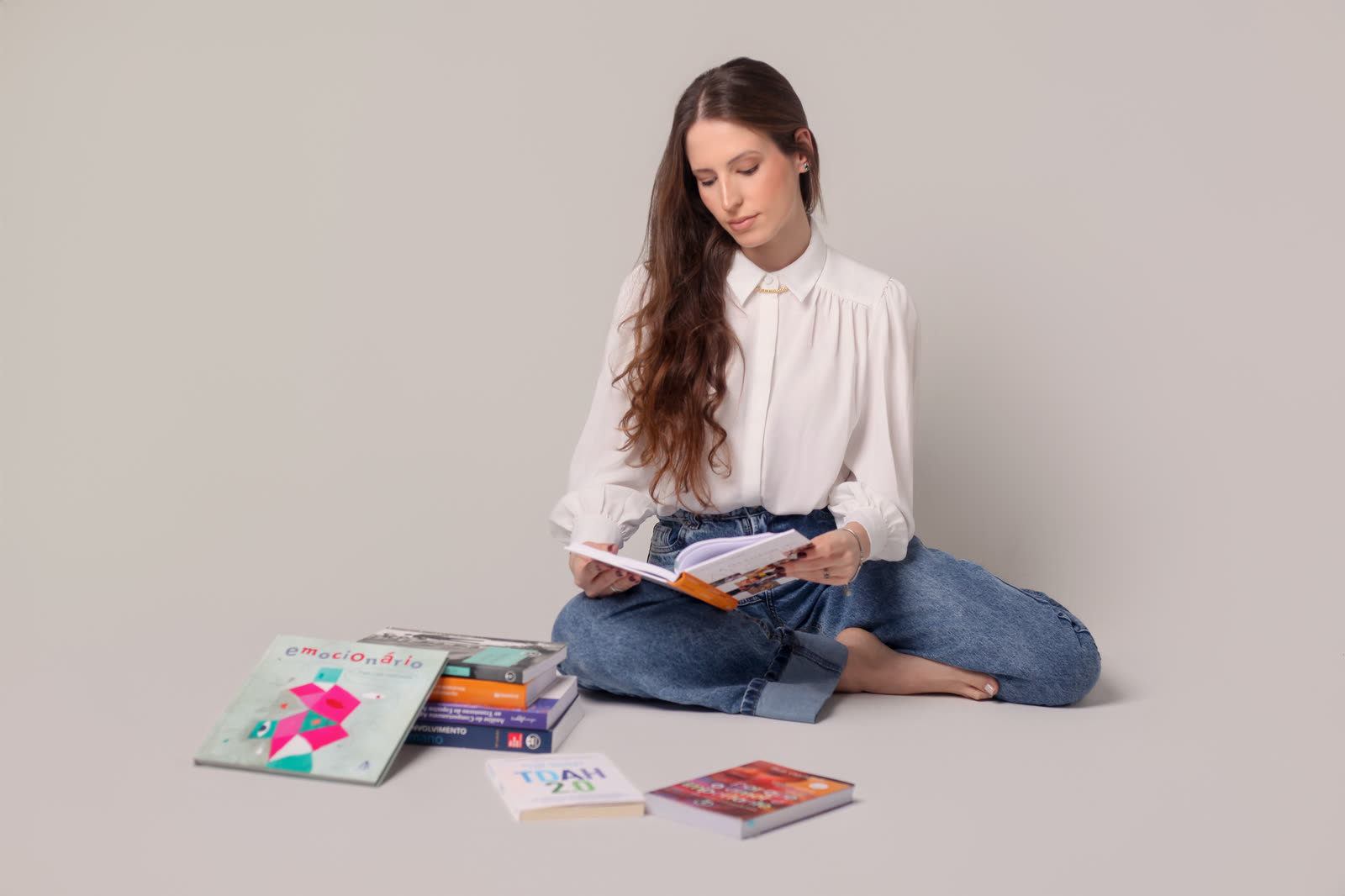 Paula Passoni sentada no chão, lendo, com livros de psicologia ao lado